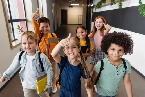 Cheerful,Multicultural,Schoolchildren,Showing,Thumbs,Up,In,School,Corridor